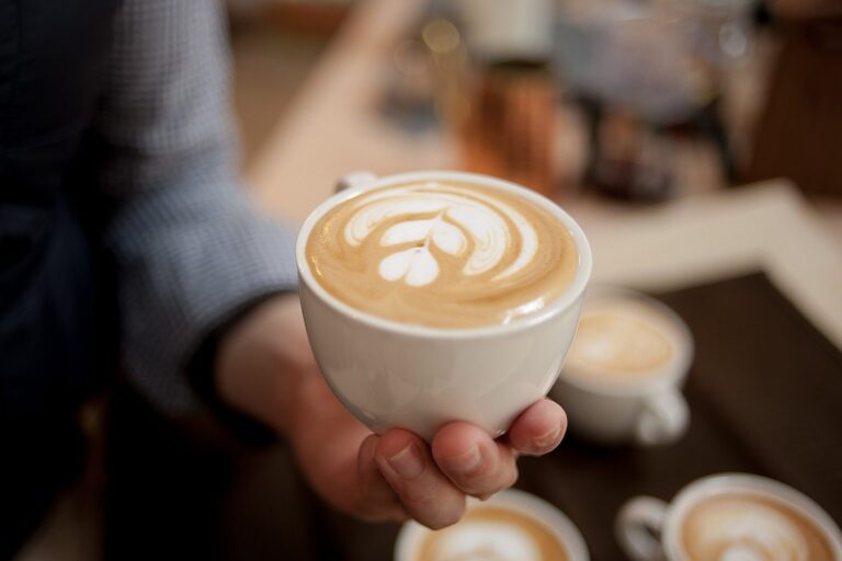Hand hält eine Tasse Cappuccino mit Latte-Art-Herz