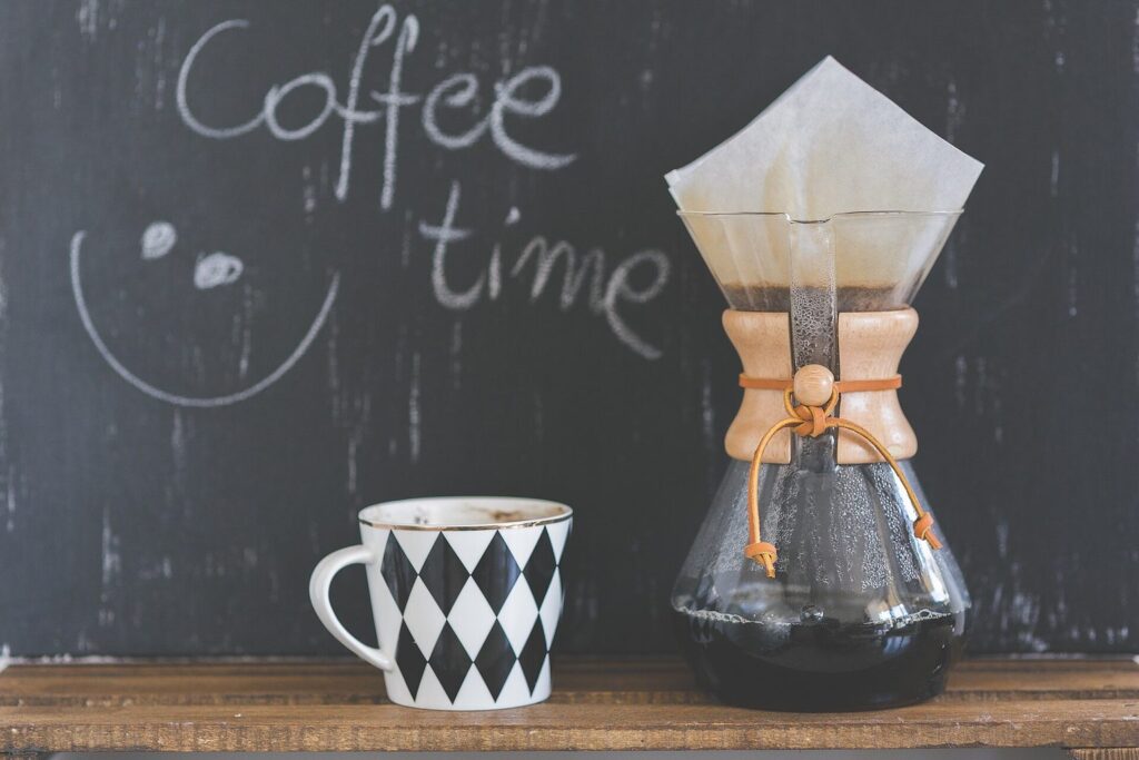 Chemex-Karaffe mit Kaffee neben einer Tasse vor einer Tafel