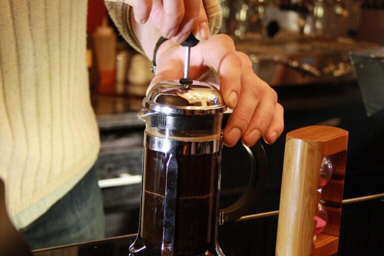 Barista drückt den Stempel einer French Press mit frisch gebrühtem Kaffee herunter