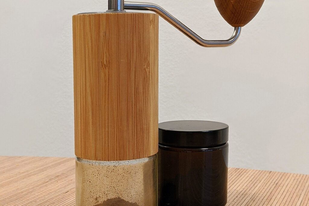 Moderne Kaffee-Handmühle mit Holzgriff neben einem Glas mit Kaffeebohnen