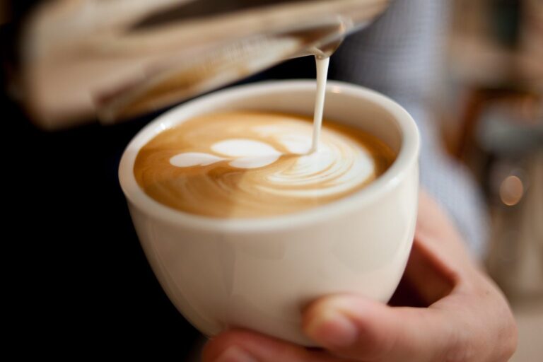 Aufgeschäumte Milch wird in eine Tasse Cappuccino gegossen und bildet ein Latte-Art-Muster