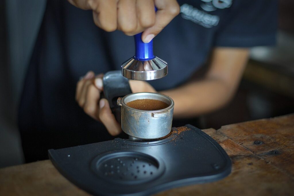 Barista tampert Kaffeepulver im Siebträger auf einer Tampermatte